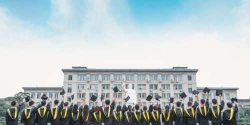 Group of graduates in gowns celebrating outdoors with a building backdrop.